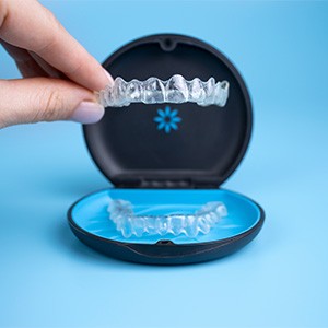 Someone lifting an Invisalign tray from the case with a light blue background