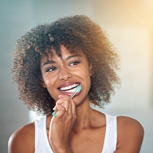 Woman in white tank top brushing her teeth in front of a mirror