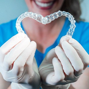 Dentist with blue scrubs and white gloves holding Invisalign in a heart shape