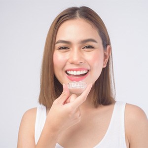 Woman with straight brown hair in white shirt inserting Invisalign smiling