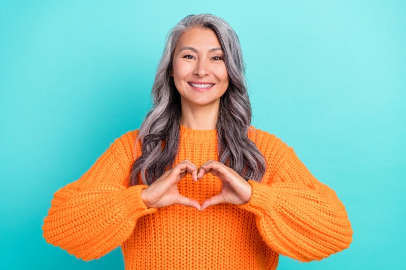 woman in orange sweater smiling and making heart shape with hands 